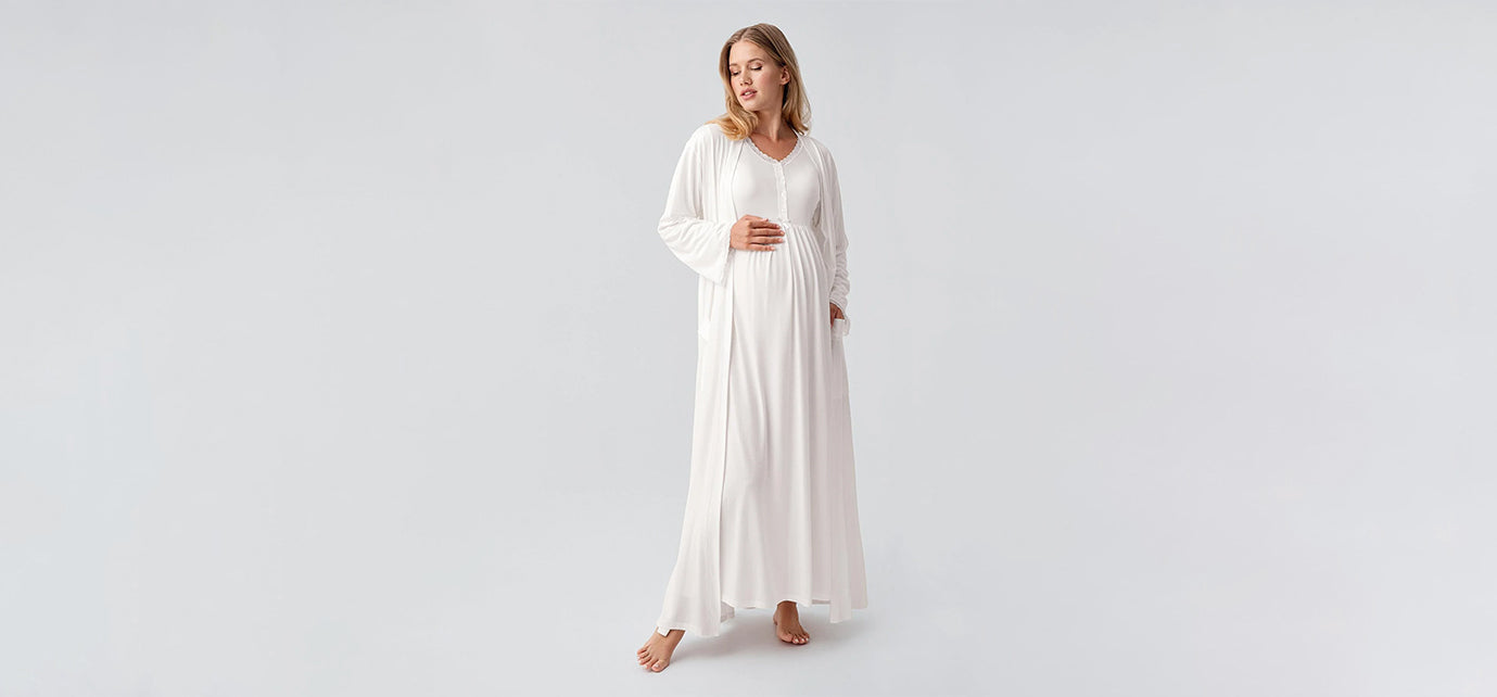 Pregnant woman in white maternity robe from Artış Collection on light background